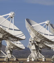 Several large parabolic radio telescope dishes stand in a row across a remote landscape, pointed toward the sky for coordinated observations.