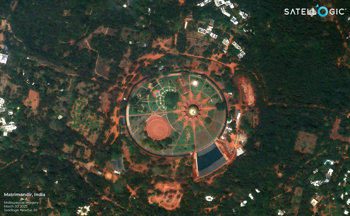A high-resolution satellite image of the Matrimandir temple in Auroville, India, showing its circular structure surrounded by gardens and greenery.