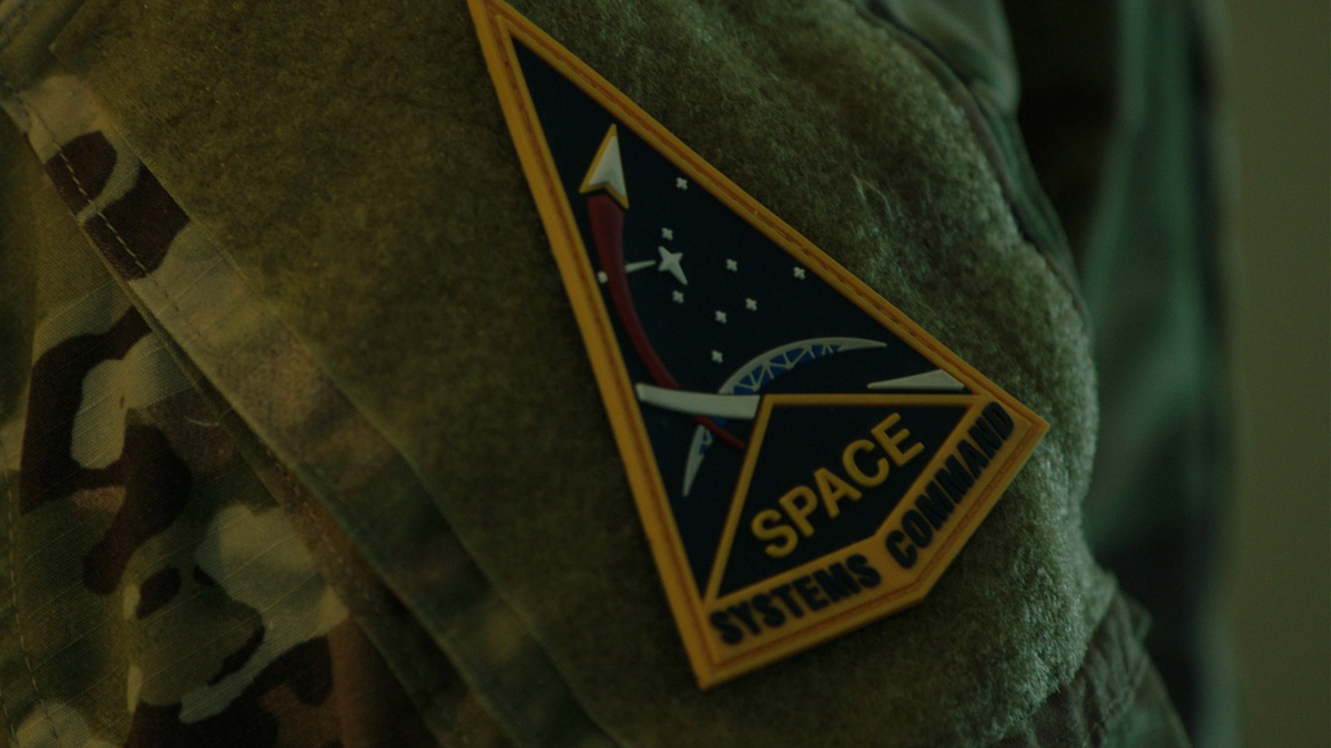 Military uniform featuring a triangular patch with a space-themed design and the words 'Space Systems Command.'