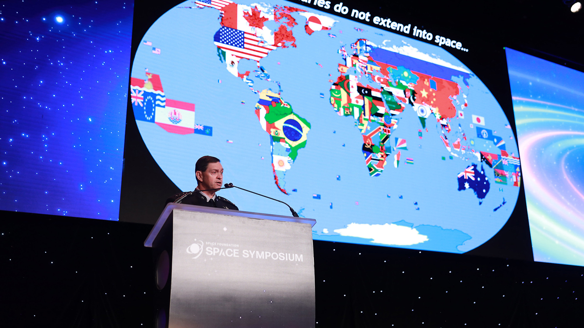 U.S. Space Force Chief of Space Operations Gen. Chance Saltzman delivers a keynote address at the Space Symposium in front of a screen displaying a map of the world with country flags. (Source: Space Foundation)