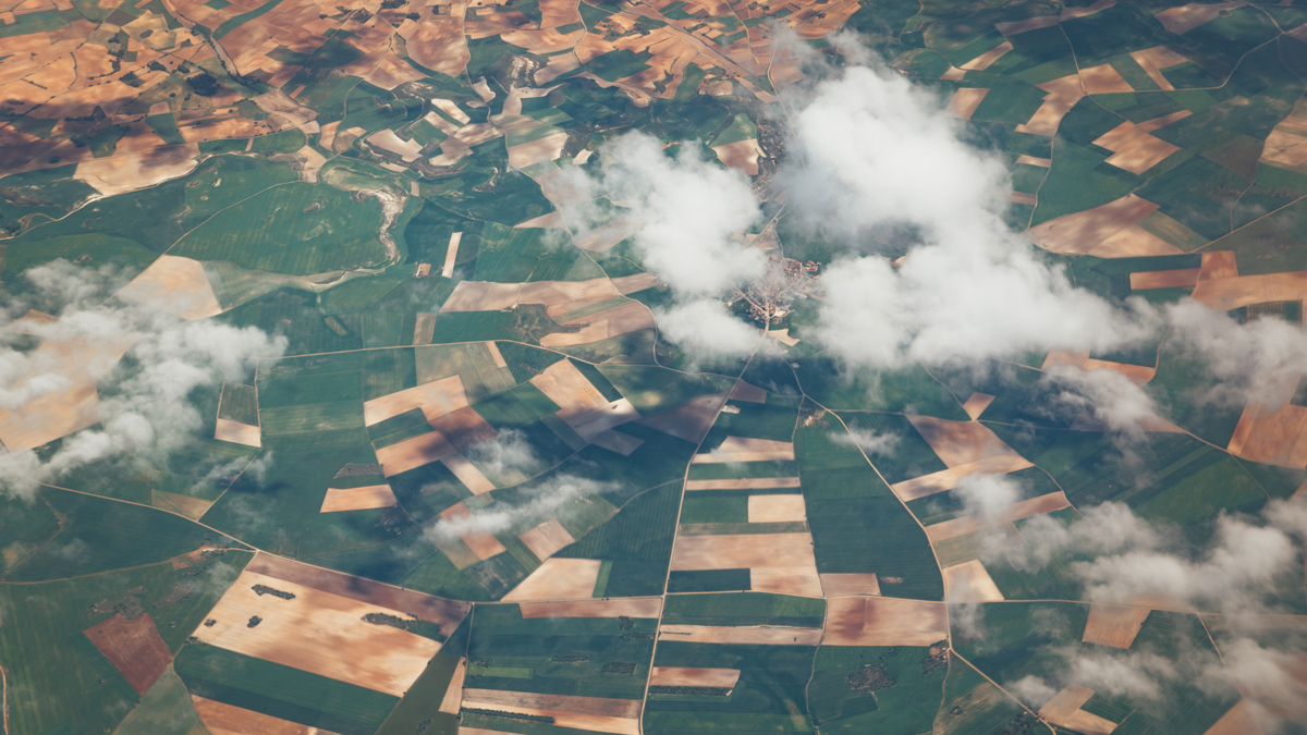 Aerial view of agricultural fields with cloud cover, captured by Earth observation satellite, highlighting SmallSat-driven big data in land use and environmental monitoring.