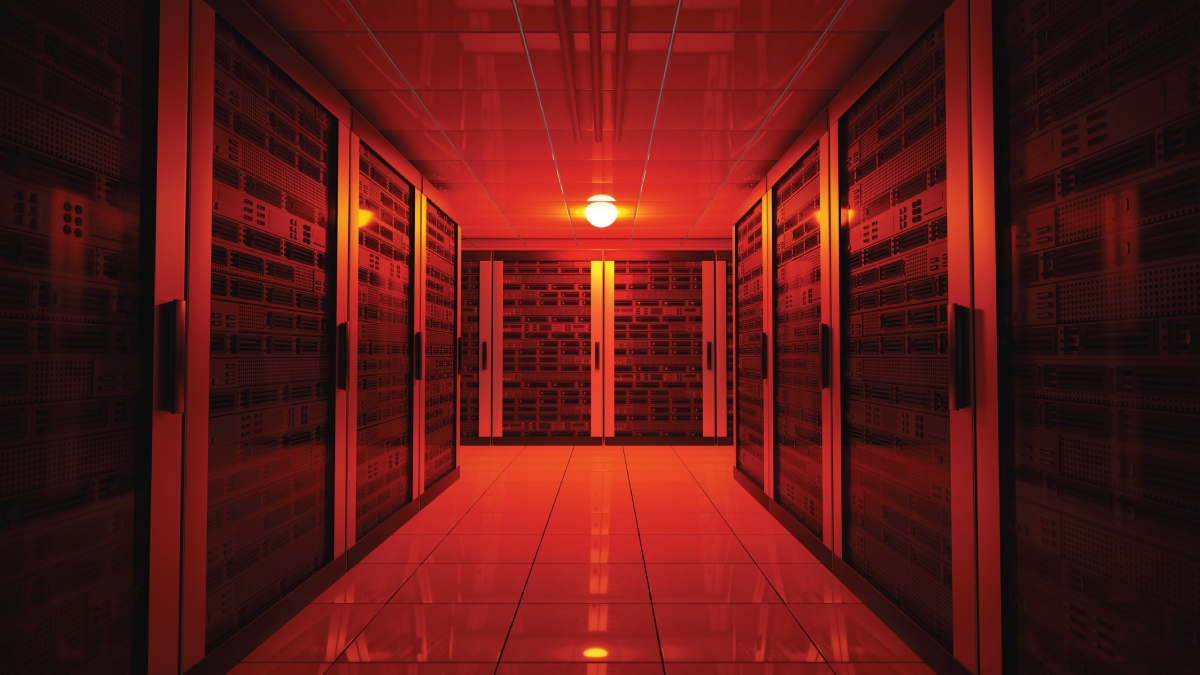 A long hallway in a data center with rows of server racks, illuminated by red emergency lighting.