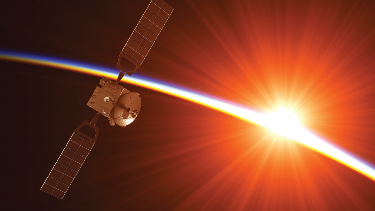 A satellite with extended solar panels orbits Earth as sunlight streams past, highlighting the planet's colorful atmospheric layer.