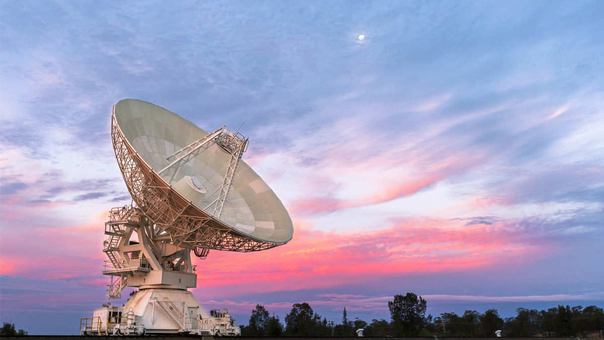 A radio telescope dish tracks the sky at sunset, demonstrating the ground-based antenna technology that enables seamless satellite communication handoffs during network failures.
