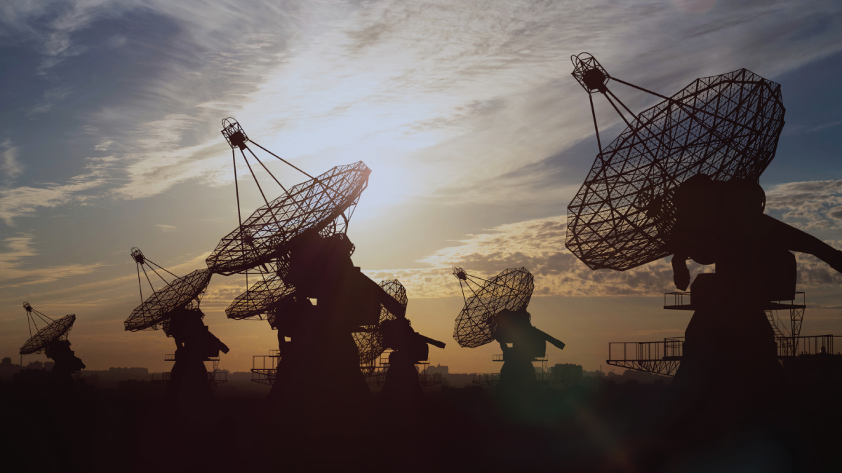 Silhouetted line of large radio telescope dishes against a dramatic sunset sky with the sun low on the horizon.