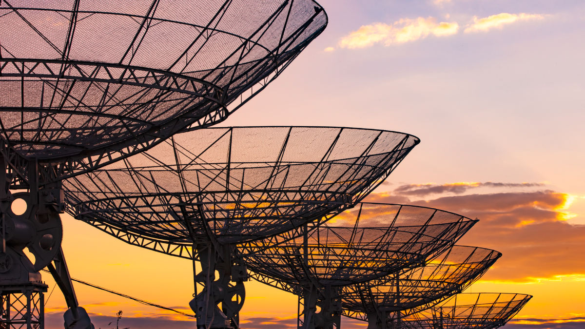 Large parabolic satellite antennas silhouetted against a sunset, representing commercial space ground infrastructure.