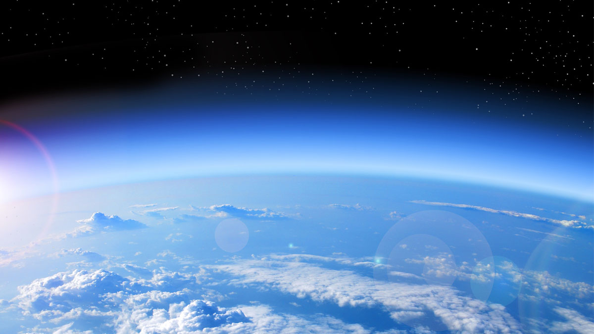 Earth viewed from orbit showing cloud formations over the planet's surface, with sunlight illuminating the atmosphere.