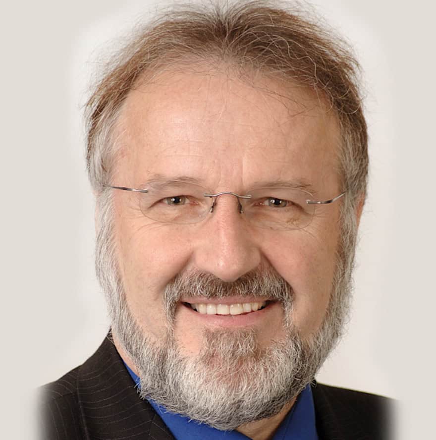 A distinguished older gentleman with a full gray beard and glasses smiling at the camera.