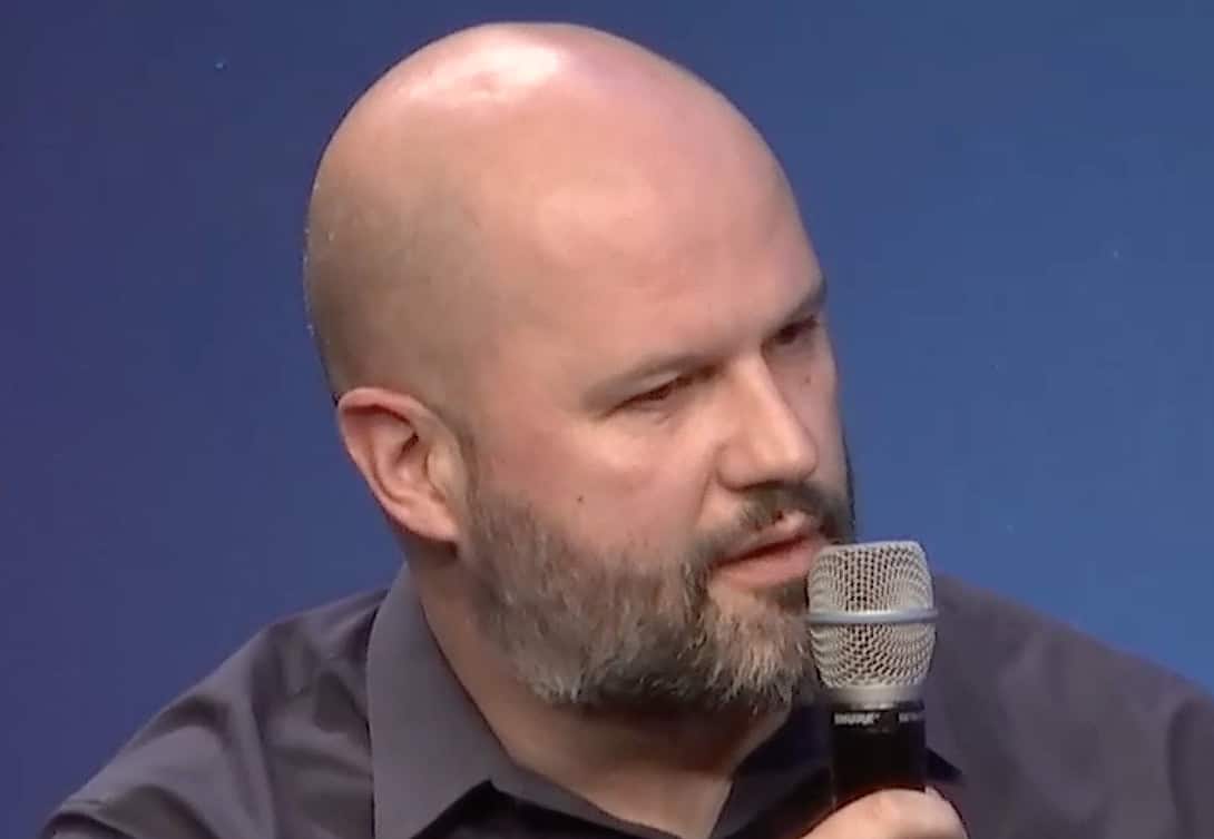 Mersad Cavcic, Globalstar chief product officer, speaking into a handheld microphone against a solid blue background.