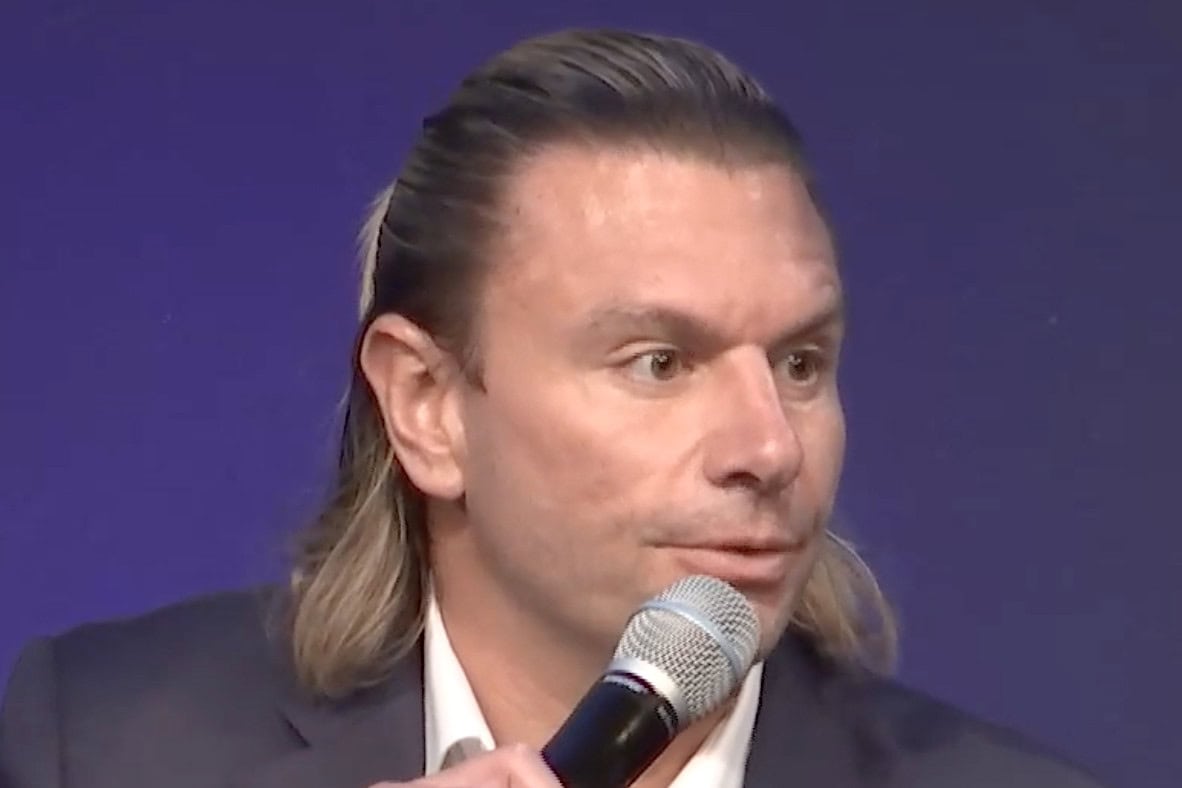 Kevin Cohen, Viasat vice president for D2D and strategic partnerships, speaking into a handheld microphone while wearing a dark blazer and white shirt against a solid dark blue background.