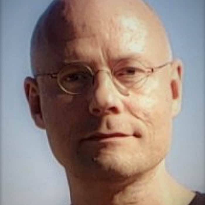 Head-and-shoulders portrait of Marko Keskinen, Skylo's managing director for Europe, a bald man wearing round eyeglasses against a clear blue sky.
