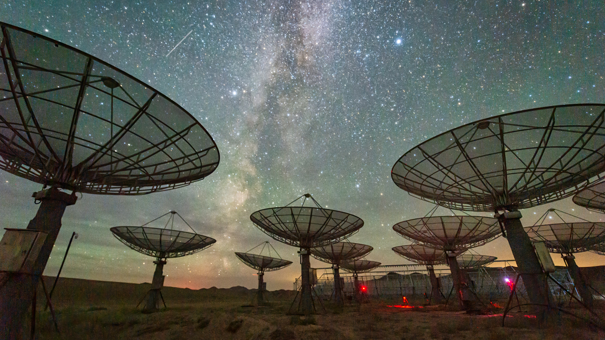 Array of large parabolic radio telescope antennas pointing upward against a brilliant night sky filled with stars and the Milky Way.