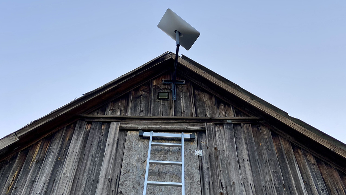 A modern rectangular satellite internet dish mounted on the peak of a rustic, weathered wooden barn, contrasting high-tech connectivity with rural infrastructure.