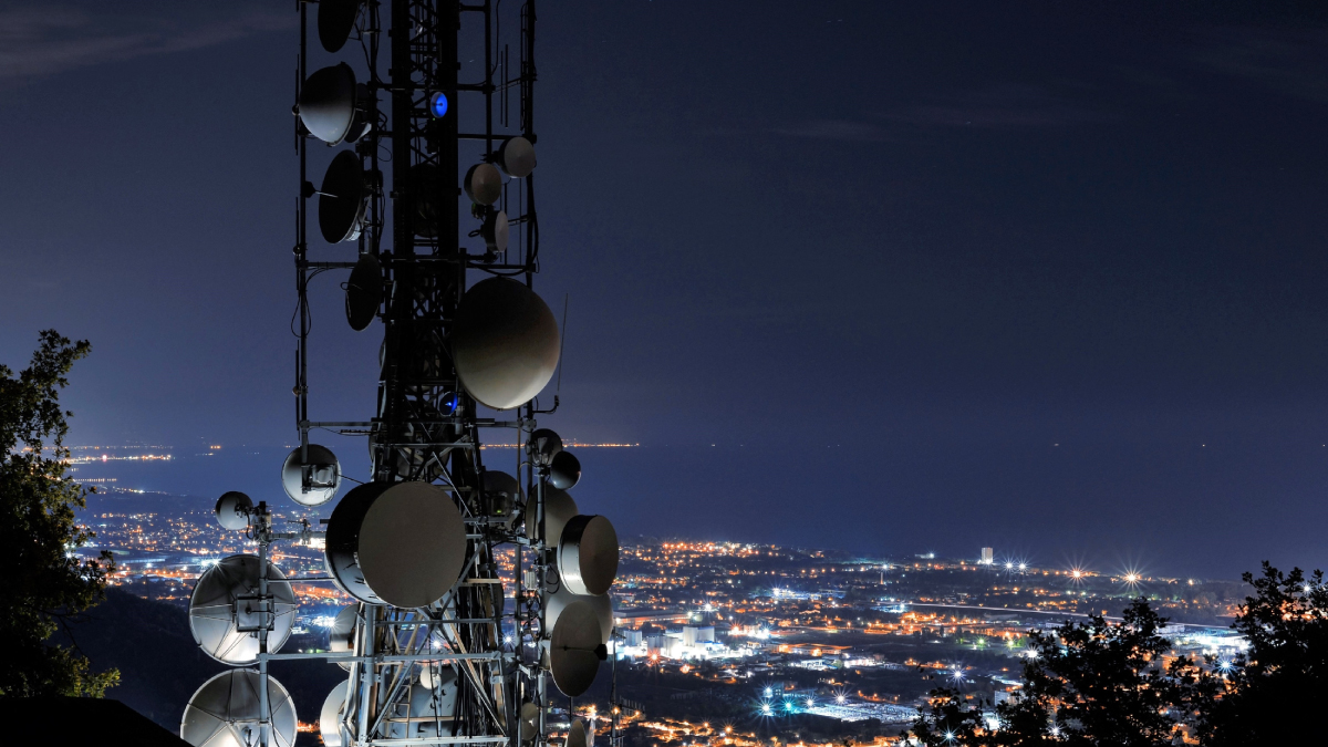 Telecommunications tower with satellite dishes overlooking a city at night, illustrating 5G NTN infrastructure.