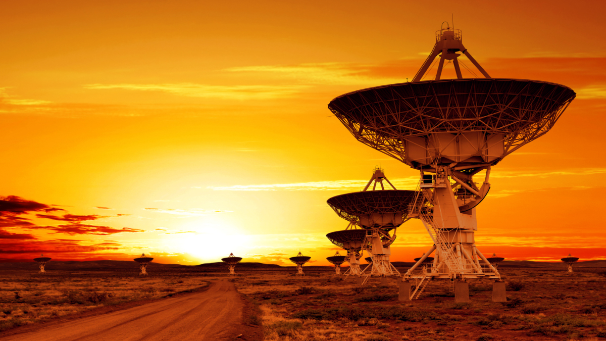 Large radio telescope array in a desert landscape silhouetted against a vibrant orange sunset.