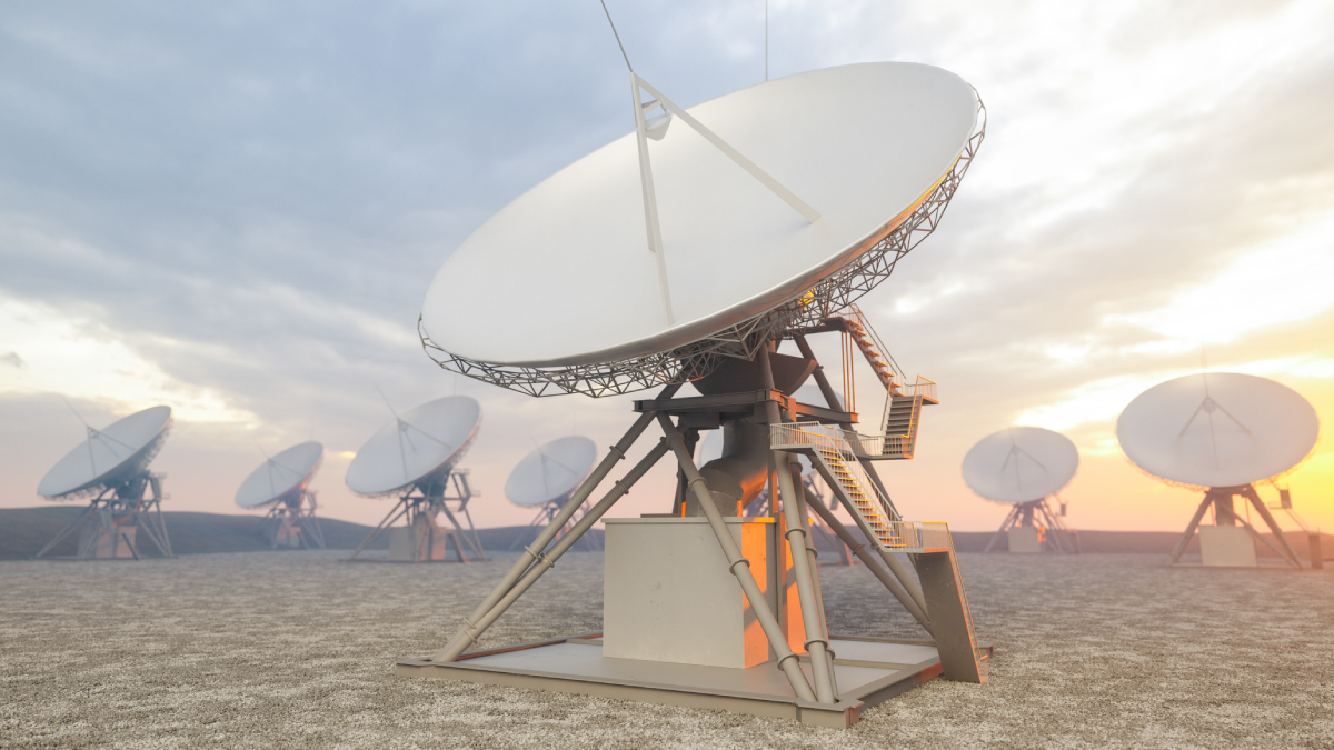 A wide field of large white parabolic satellite antennas stands on a flat, gravel plain under a hazy, warm sky at sunrise.