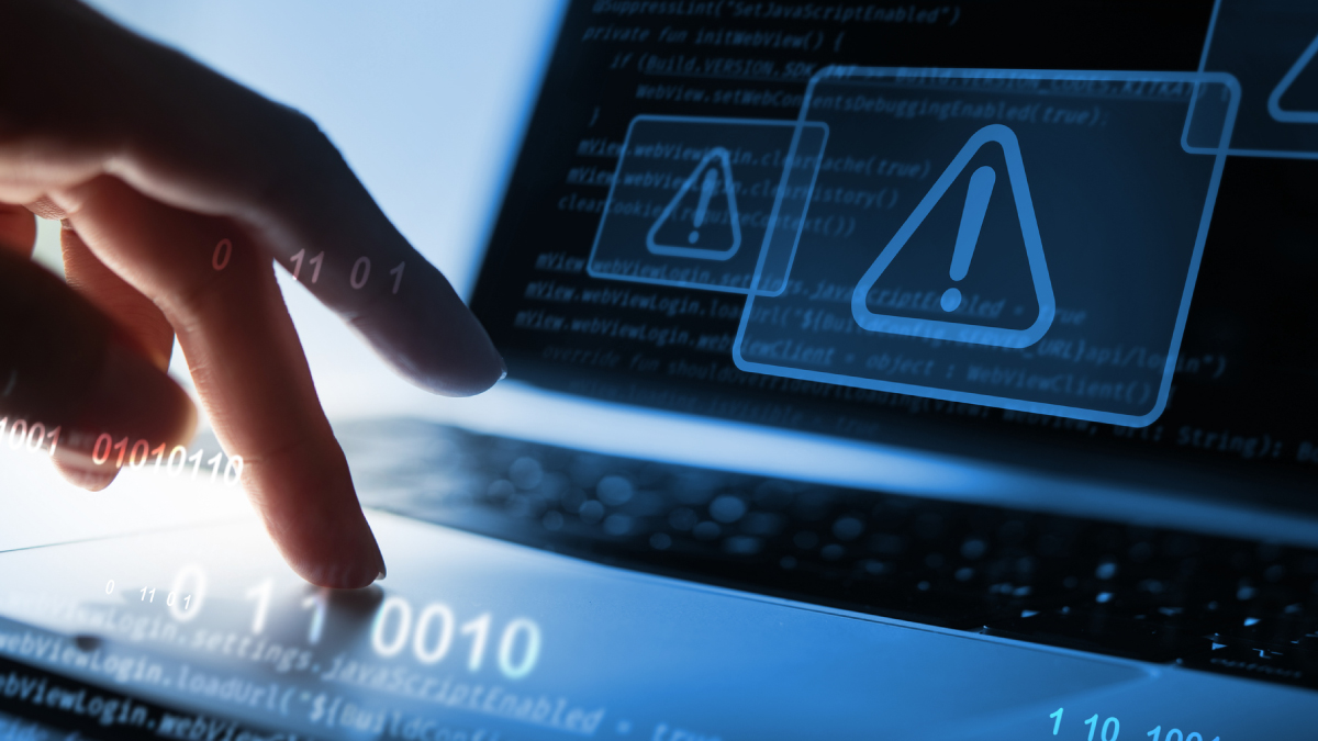 A close-up of a hand pressing a key on a laptop keyboard, overlaid with glowing blue binary code, programming scripts, and digital warning triangle icons.