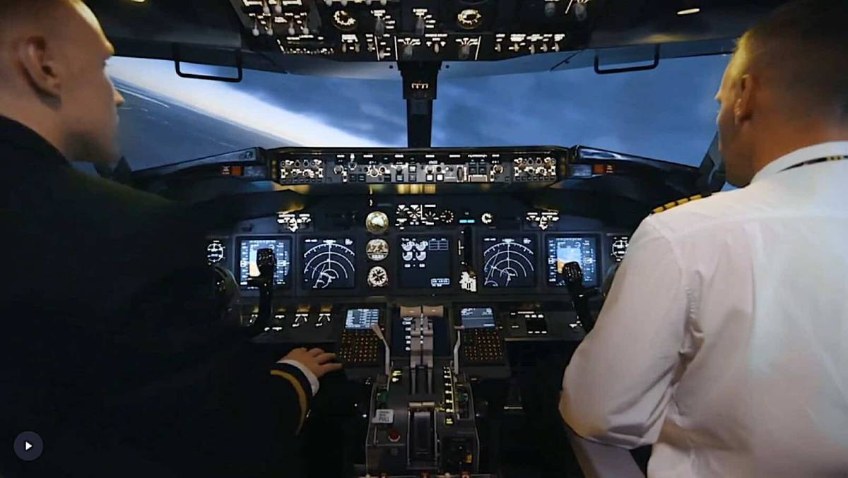 Two pilots sitting at the illuminated instrument panel inside the cockpit of a commercial airplane during a flight.