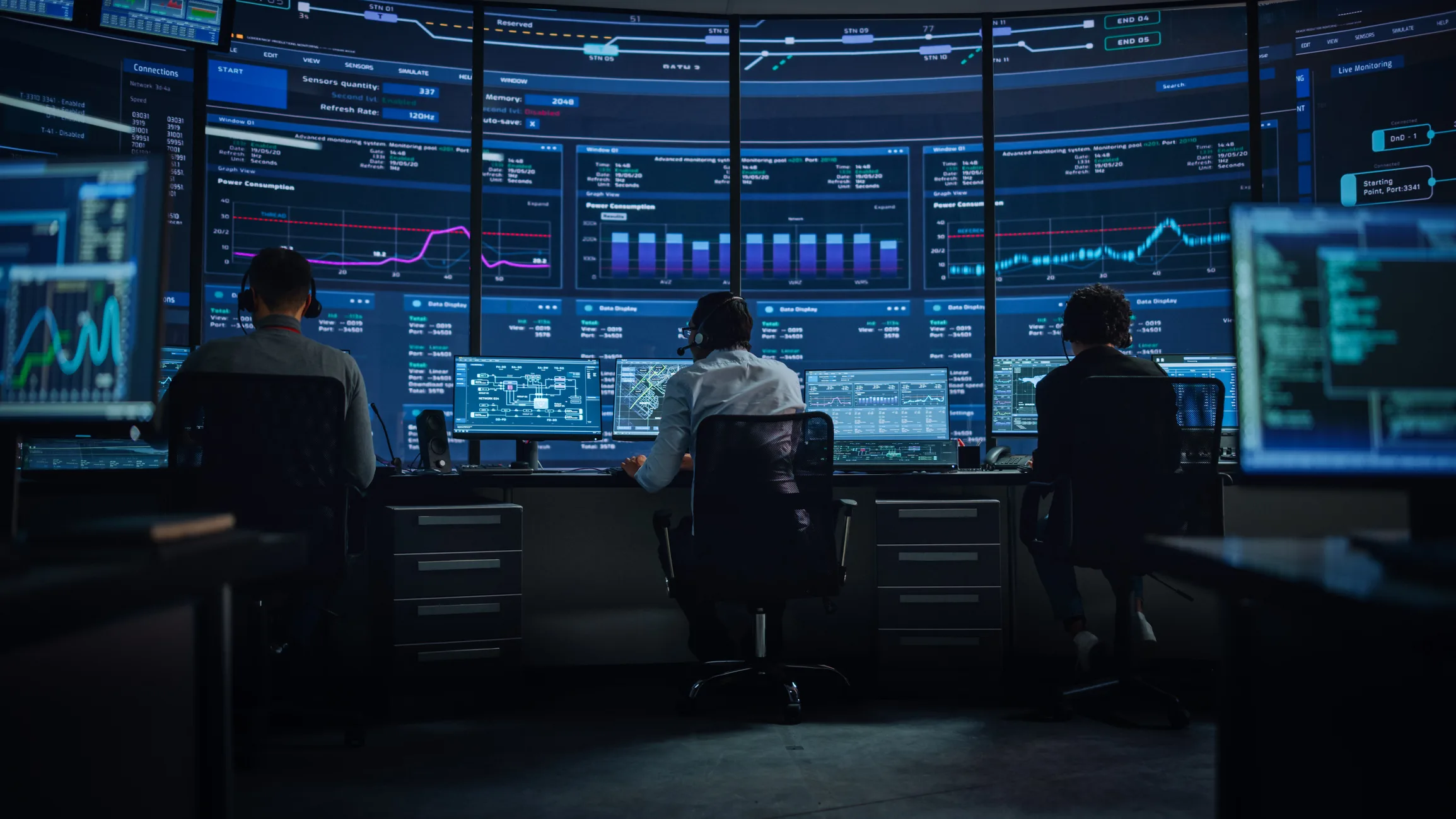 Operators in a modern Kratos satellite network operations center monitoring real-time signal processing telemetry, spectrum performance graphs, and system metrics across wall-mounted displays.