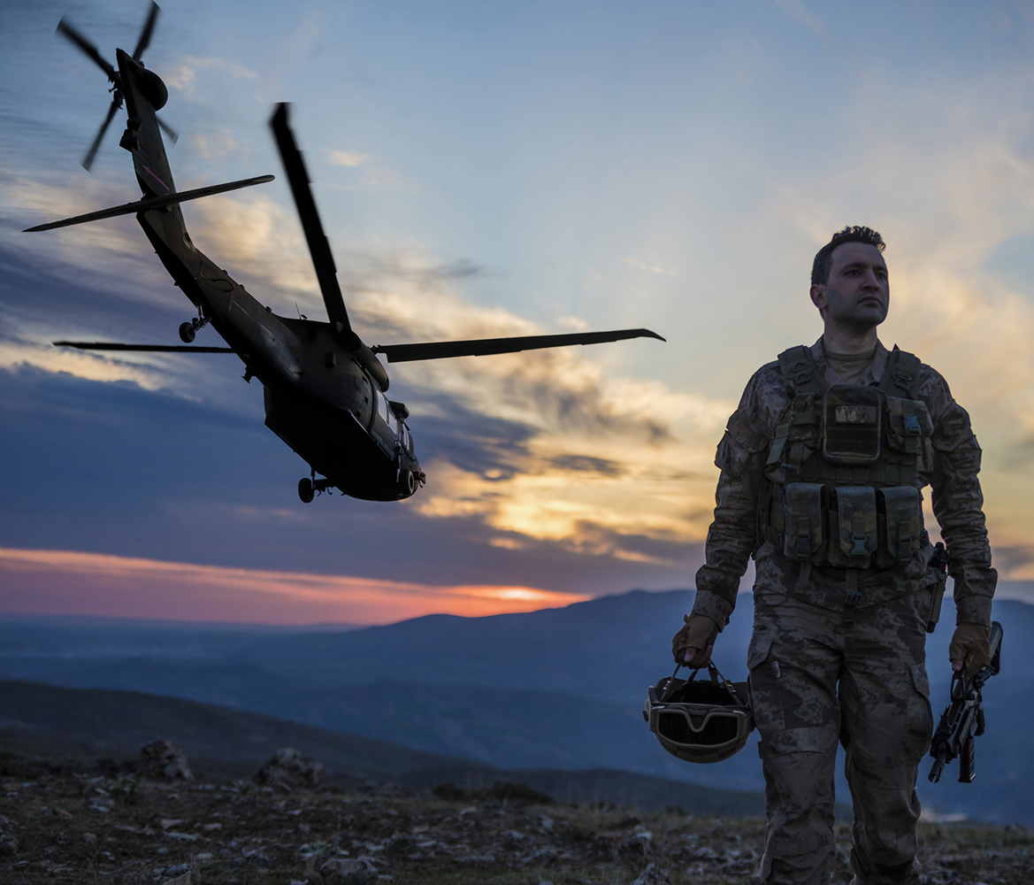 Tactical operator in gear standing beside flying helicopter during sunset operation.