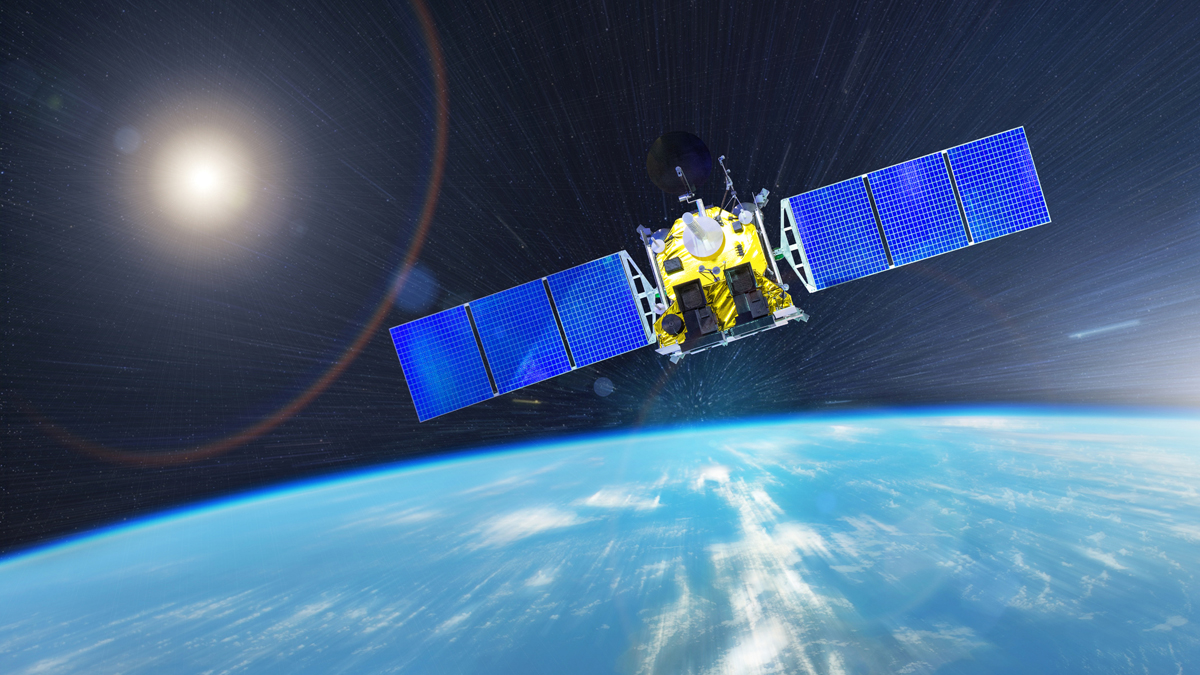 Gold foil-insulated communications satellite with extended solar panel arrays orbiting high above the Earth with bright sun flare.