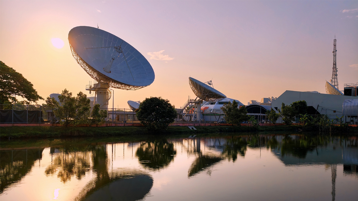 Large parabolic satellite ground station antennas reflecting in a calm pond during sunset.