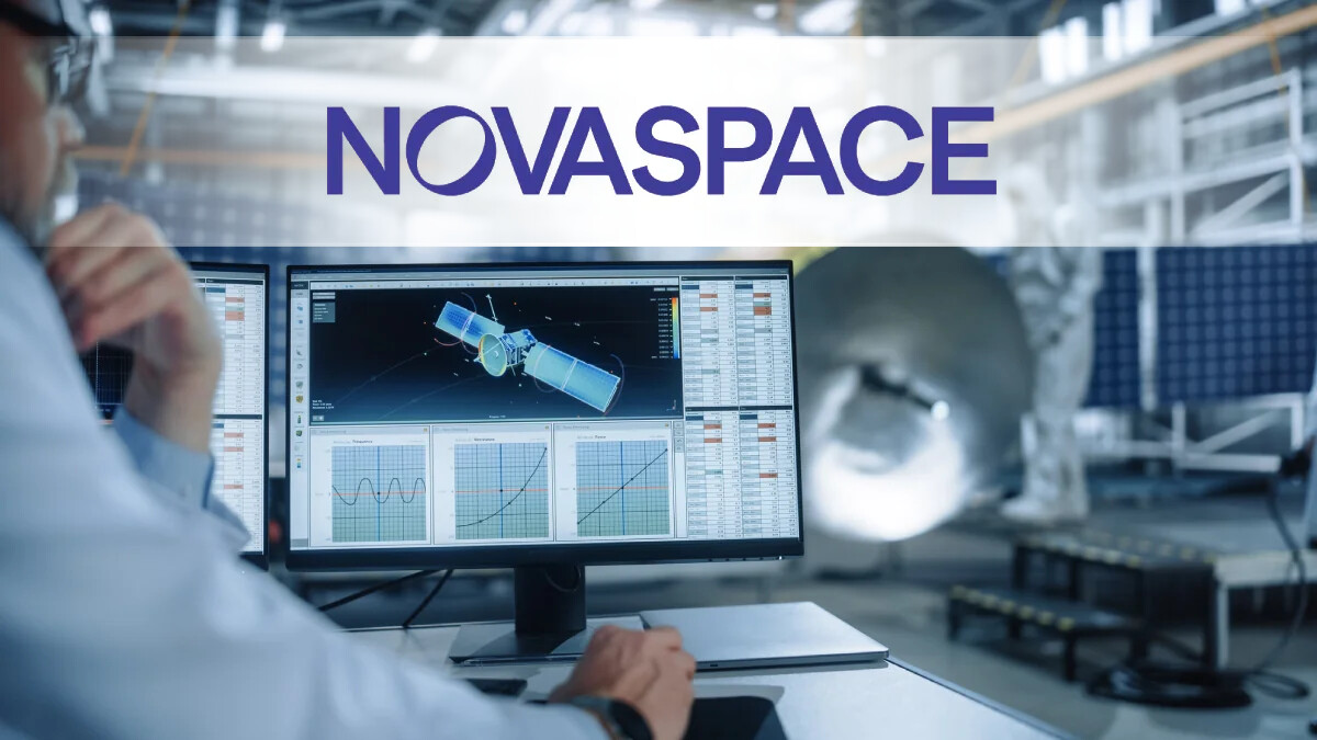 An engineer monitors a 3D model and telemetry graphs of a satellite on a computer screen inside a high-tech aerospace manufacturing facility.