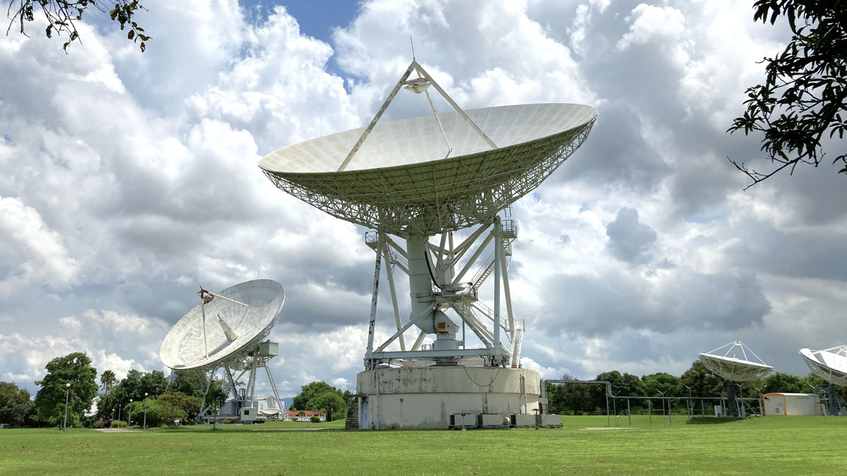Array of large parabolic satellite ground station antennas under a partly cloudy sky.