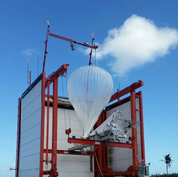 A Google Loon balloon being prepared for launch from a specialized platform under a clear blue sky.