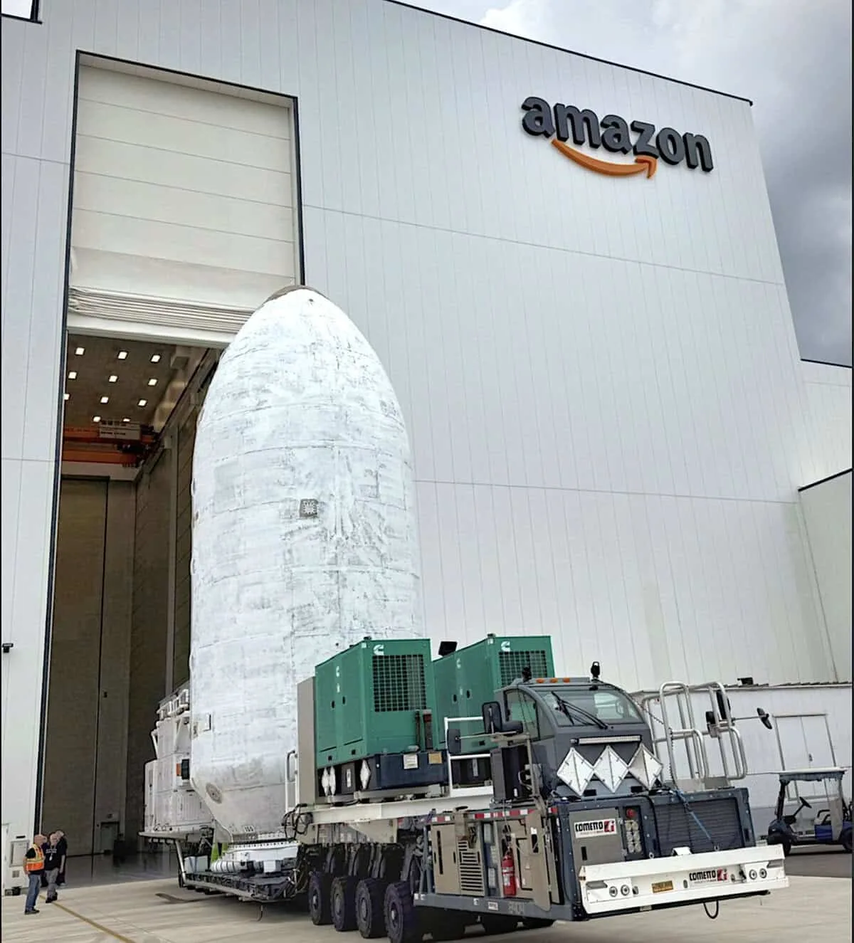 Rocket payload fairing carrying Project Kuiper satellites on a transport vehicle outside an Amazon satellite processing facility.