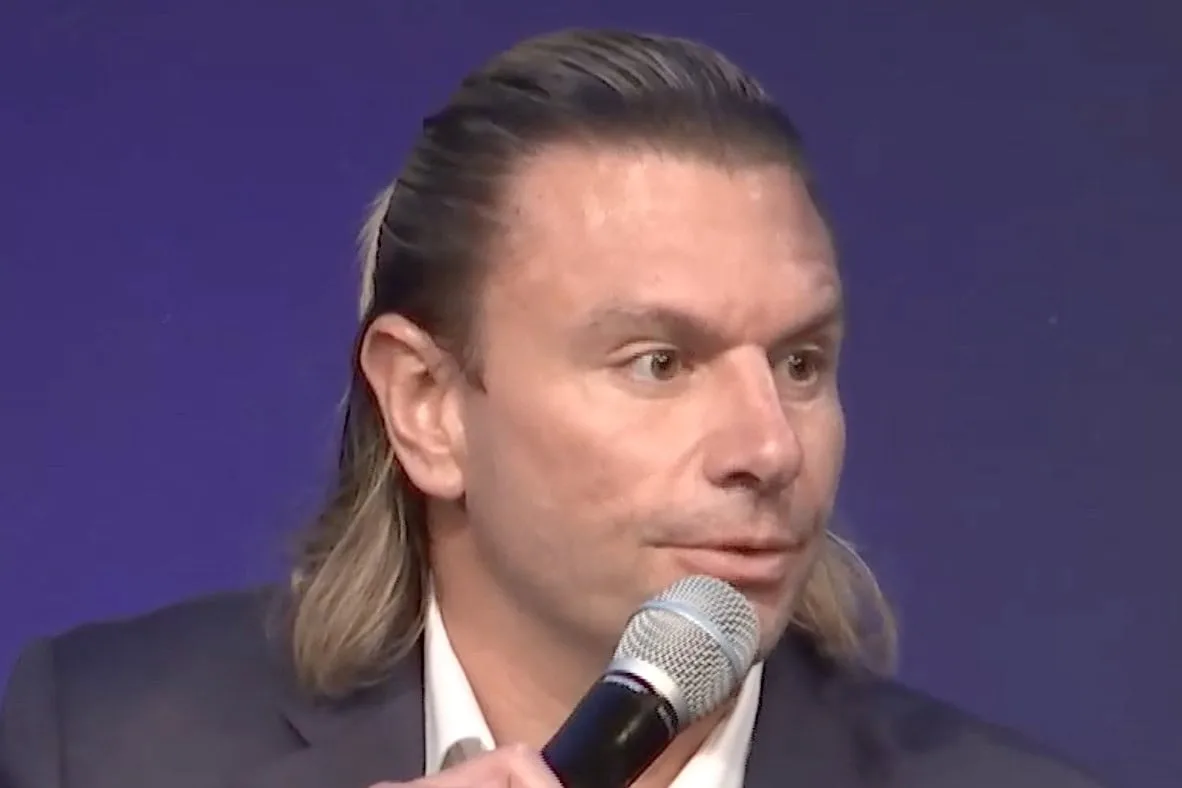 Kevin Cohen, Viasat vice president for D2D and strategic partnerships, speaking into a handheld microphone while wearing a dark blazer and white shirt against a solid dark blue background.