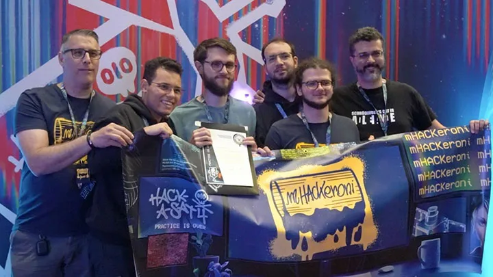 Hack-A-Sat 4 winning team 'mHACKeroni' displays their banner and shows off their award for capturing first place during the two-day competition, Aug. 11-12 in the Aerospace Village at DEF CON 31 in Las Vegas.